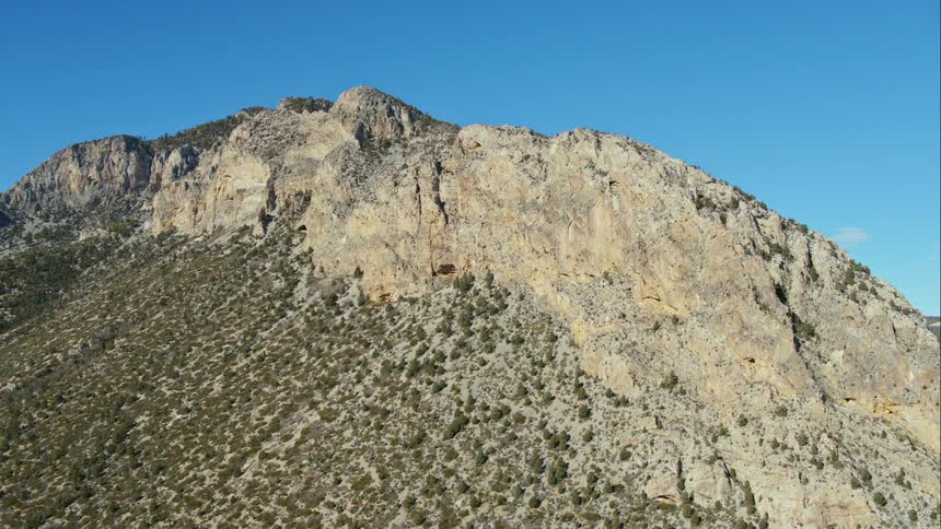 A mountain covered in shrubs and surrounded by a bright blue sky