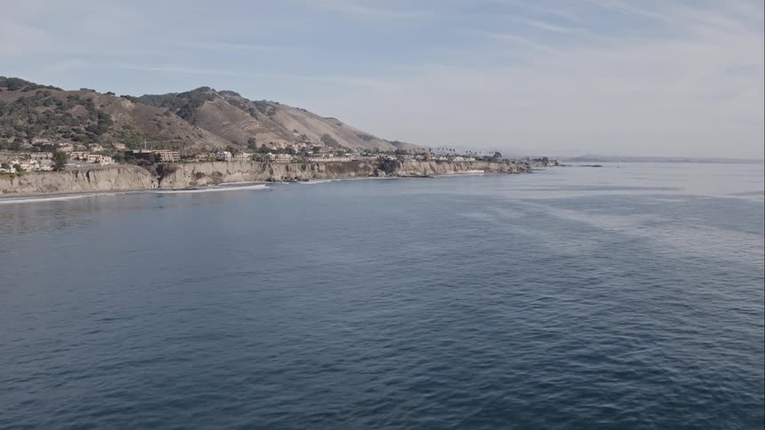Aerial of a calm sea near a cliff side neighborhood on an island