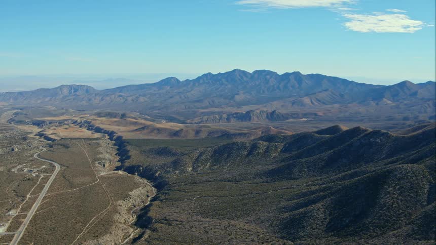 A mountain range looms over a valley containing a road and a few small structures