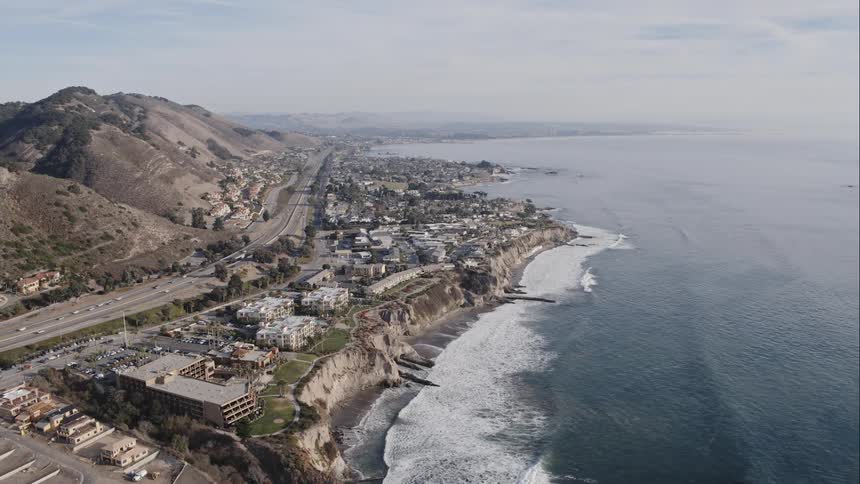 Aerial shot of a highway on the coast with houses cliffs and breaking waves