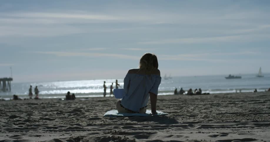 A woman sits alone on a populated beach on a cloudy day