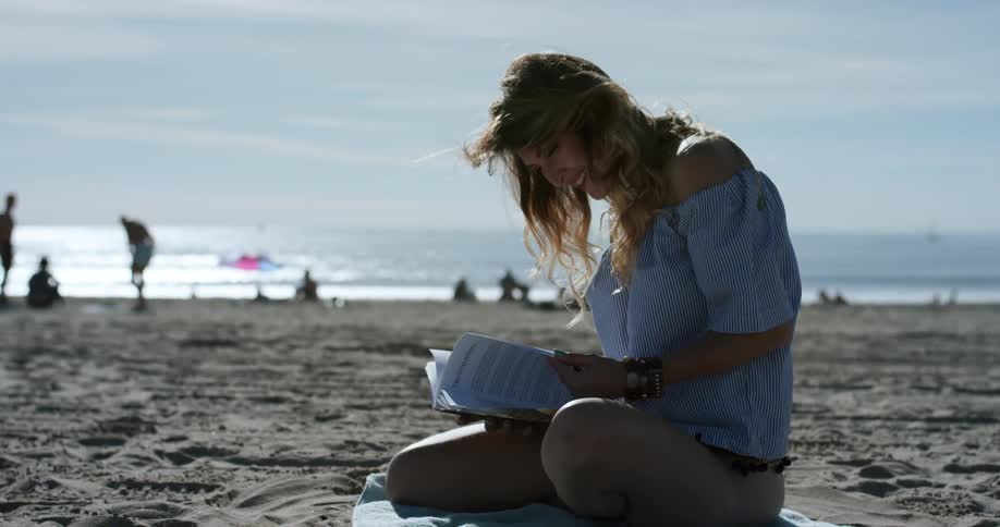 A woman sits on a towel on the beach while reading