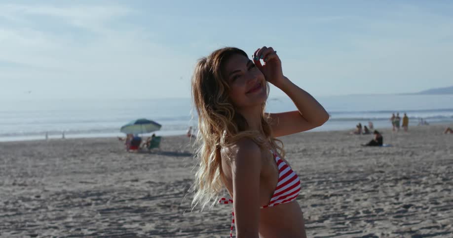 Woman wearing bikini poses for the camera on the white sand beach next to the sea