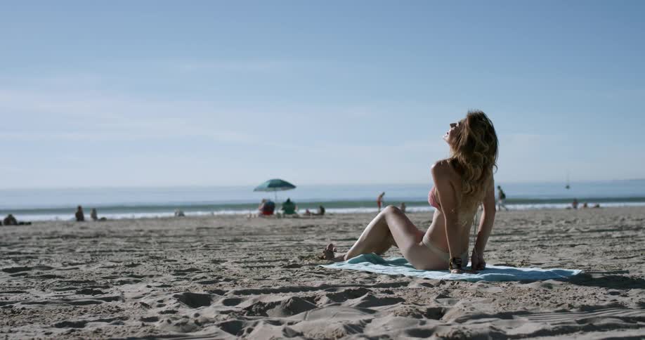 A young white woman in a bikini sunbathes on a beach