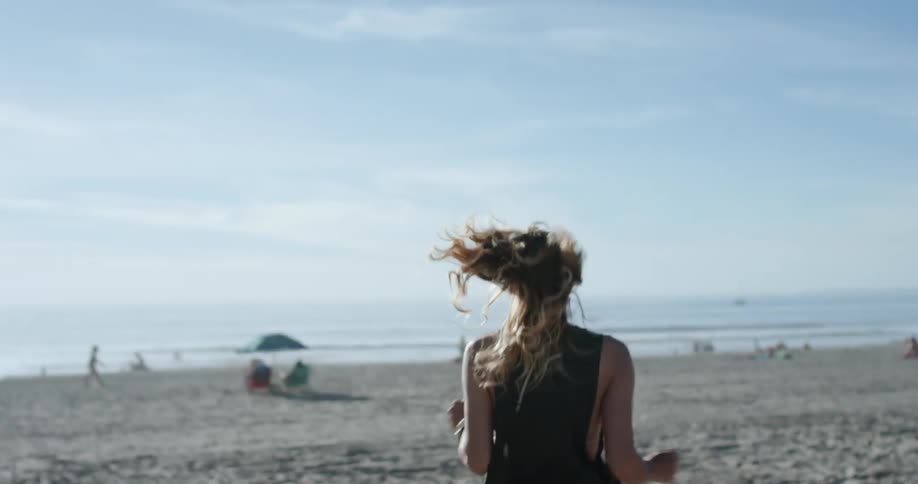 A woman with blonde hair runs through the sand towards the ocean
