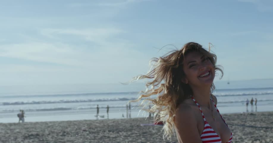 A woman smiles while wearing a red striped bikini on a sandy beach