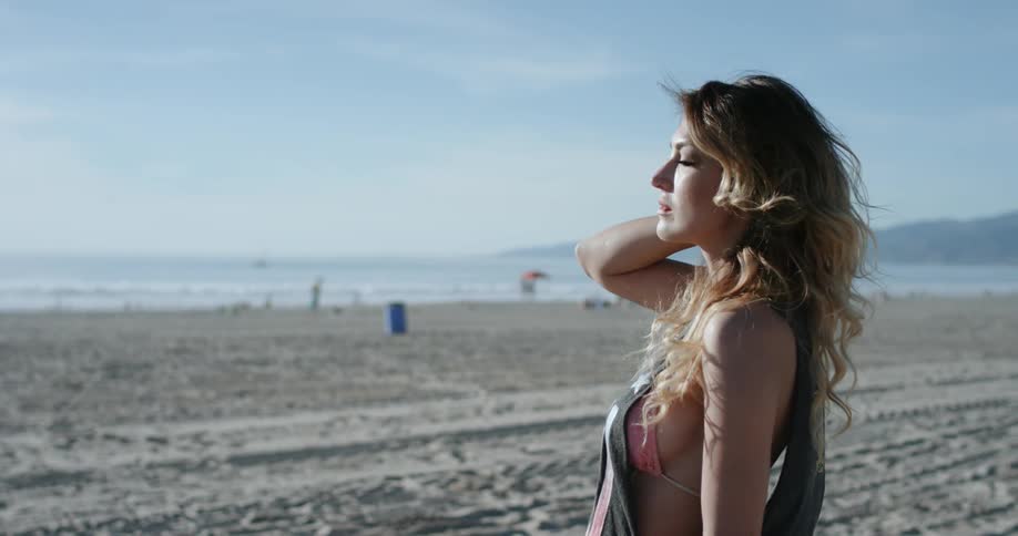A woman runs her hair through her hands while standing on a beach