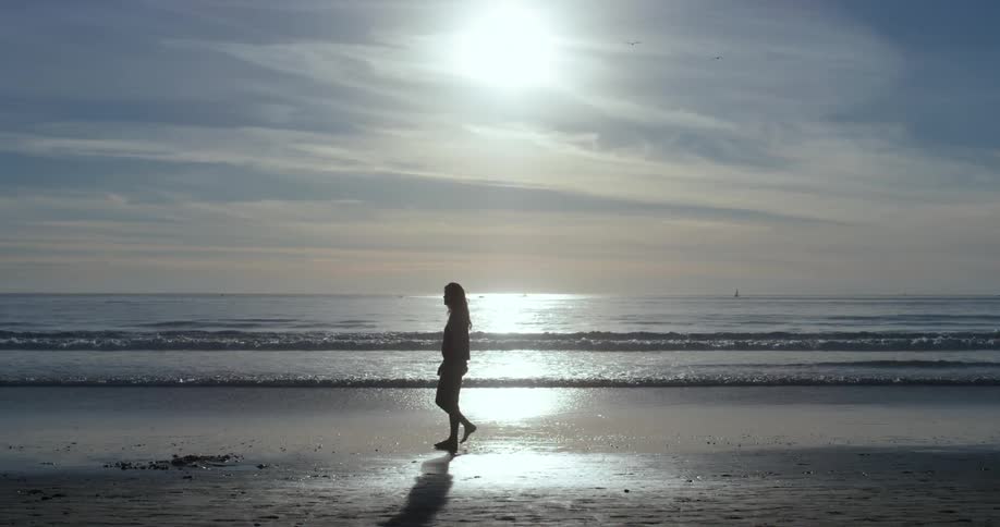 A woman walks along the beach under the sun