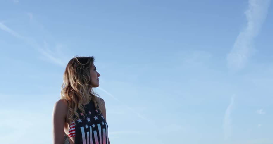 A woman wearing a tank over a bikini top looks around and shakes her long hair