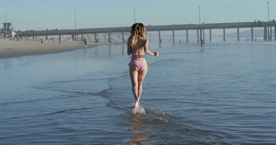 A woman in a bikini running along the beach in water