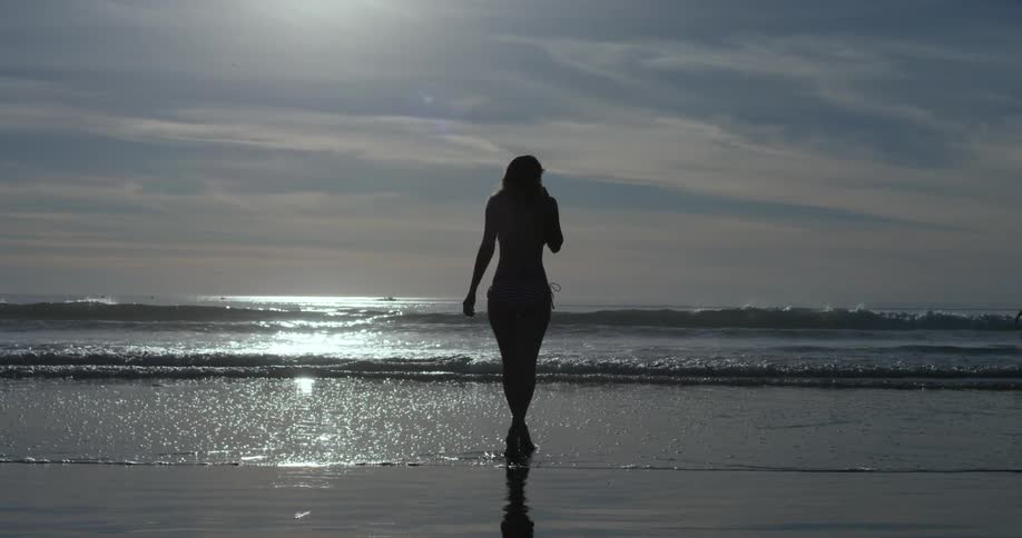 A woman in a bathing suit walks across the beach and into the water