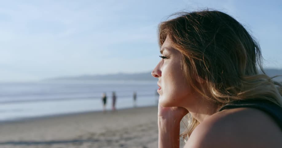 A woman sitting on the beach looks off to the water