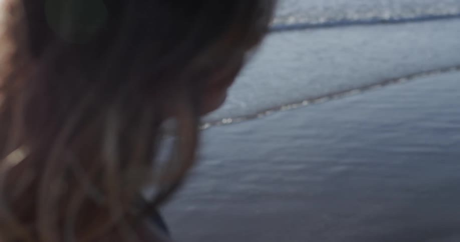 A white woman stands on the beach and looks at the waves washing ashore