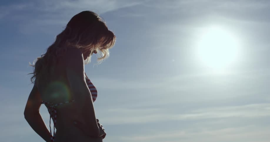 Woman wearing bikini stands hands on hips under the sunlight