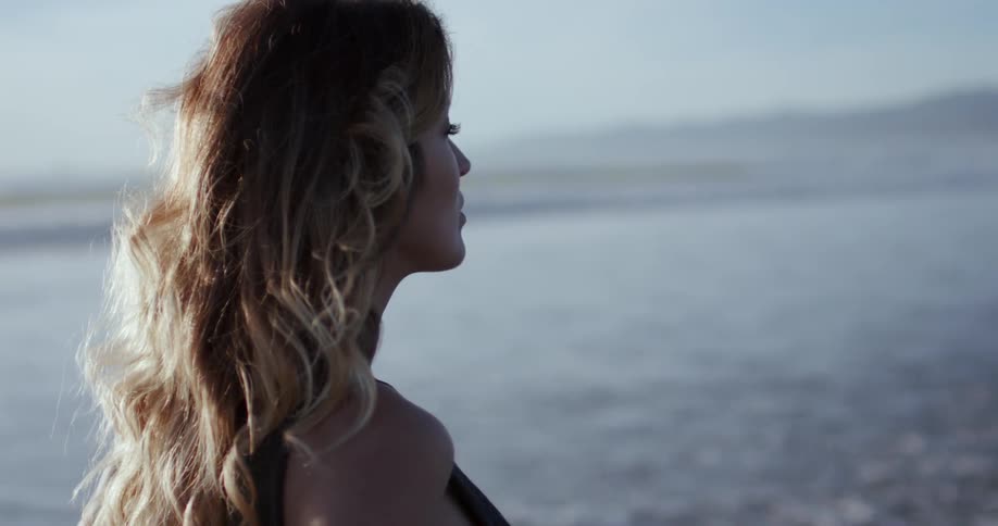 A woman stands by the surf and watches the ocean