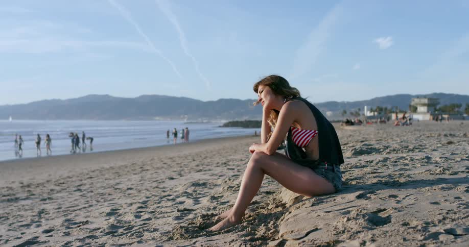 A young girl sits on the beach and looks towards the water
