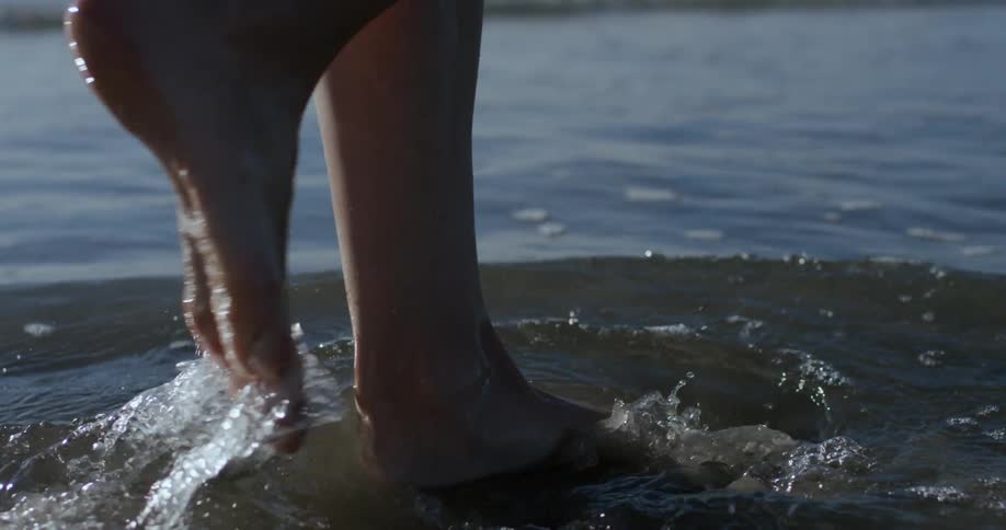 Woman walks barefoot along the sea and splashes water during daylight