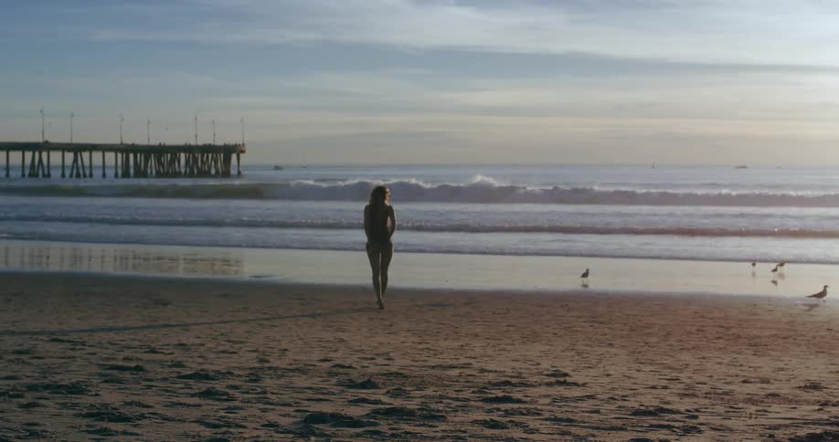 A woman walks along a beach toward the ocean