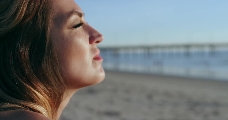 A woman runs her hand through her hair while at the beach