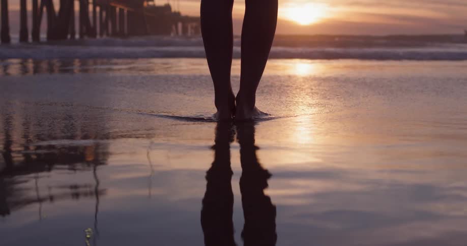 A person standing on a beach with shallow waves washing over their feet