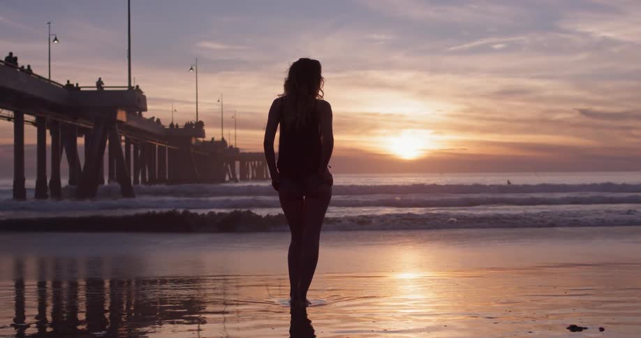 A woman stands beside the coast at dusk