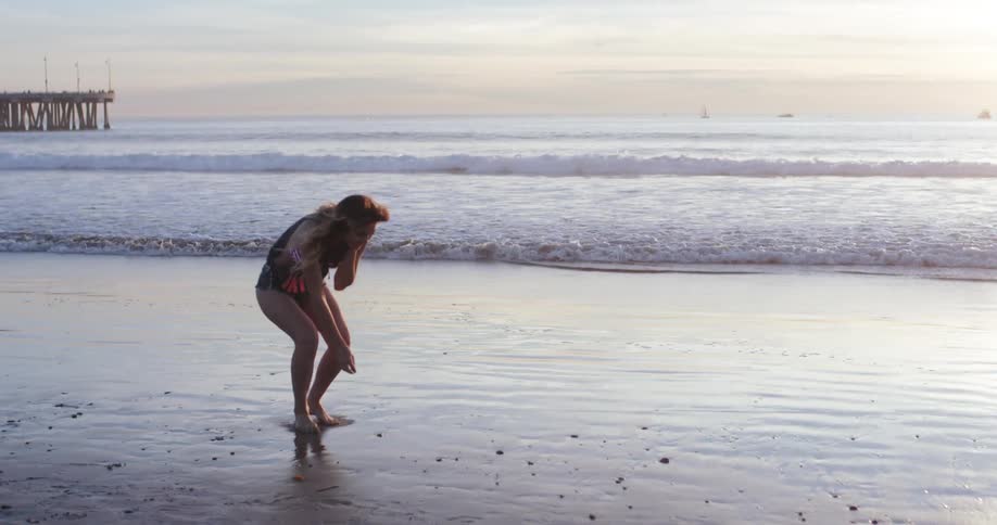 Woman walking barefoot on a beach next to a pier at sunset