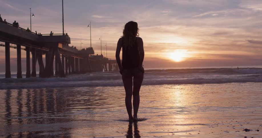 A woman stands on a beach looking at the sunset