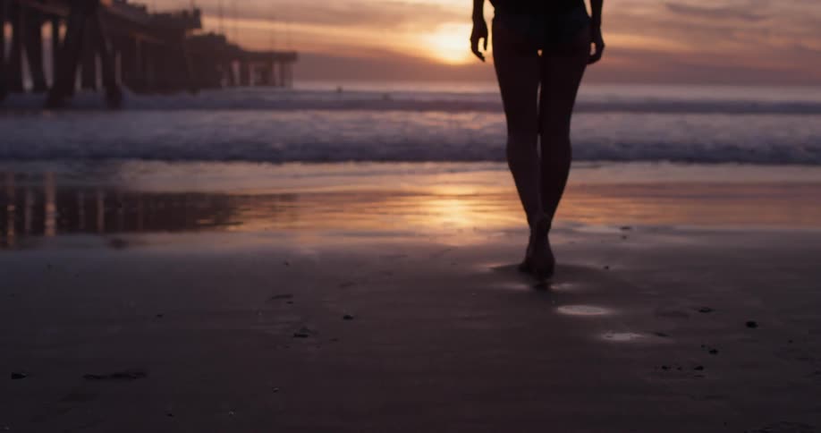 A woman slowly walks on a deserted beach as the sun sets