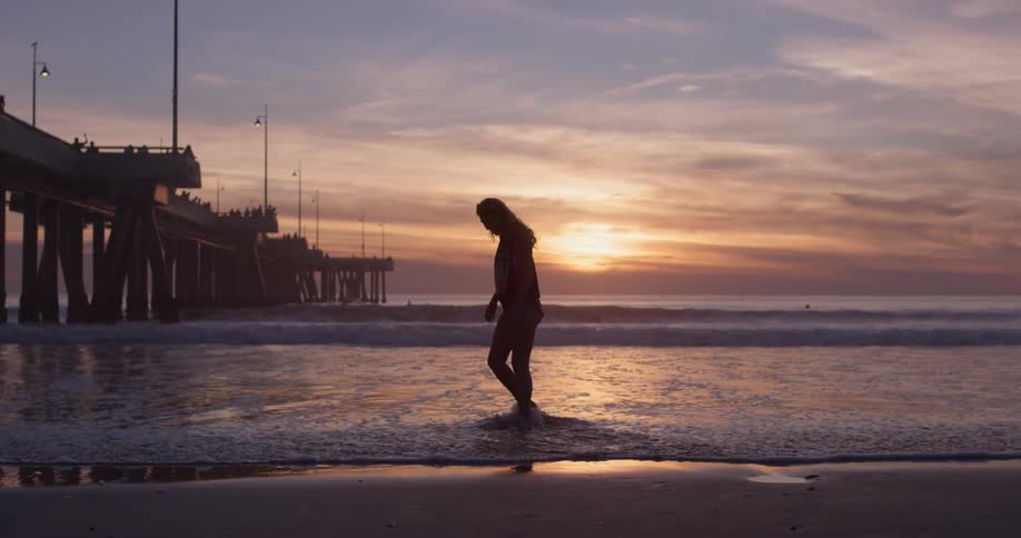 A woman splashes her feet through shallow water on the beach