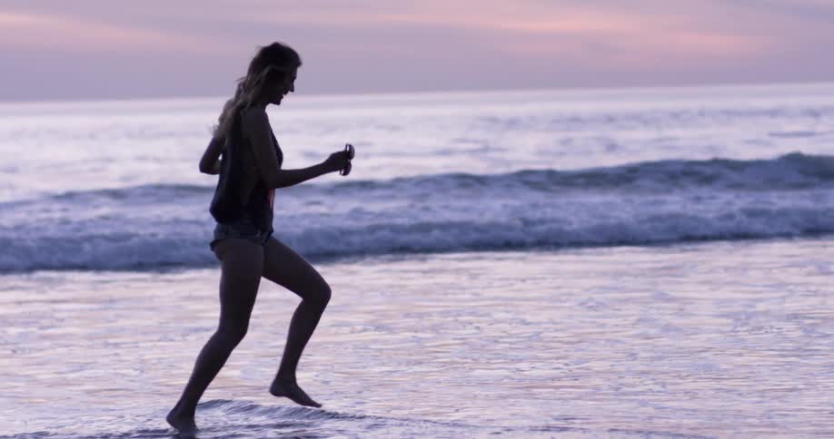 A woman in denim shorts and a bikini runs on a beach at sunset
