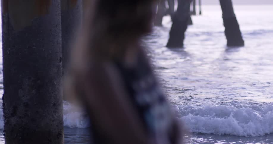 A woman stands underneath an oceanside pier