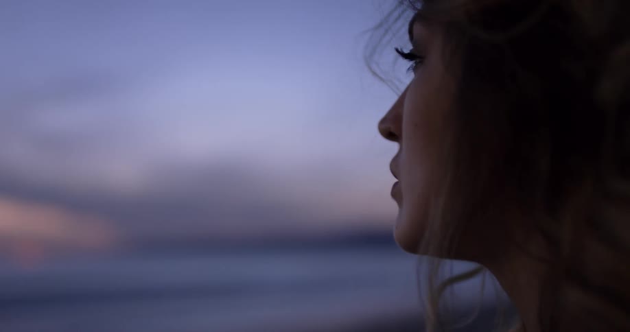 A white woman looks out at the ocean while standing on the beach