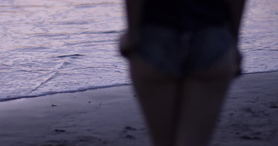 A woman with daisy dukes standing on the beach looking at the ocean
