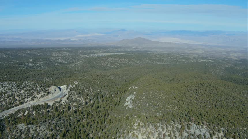 A long paved road can be seen carving its way through a canyon in the midst of an expansive forested area