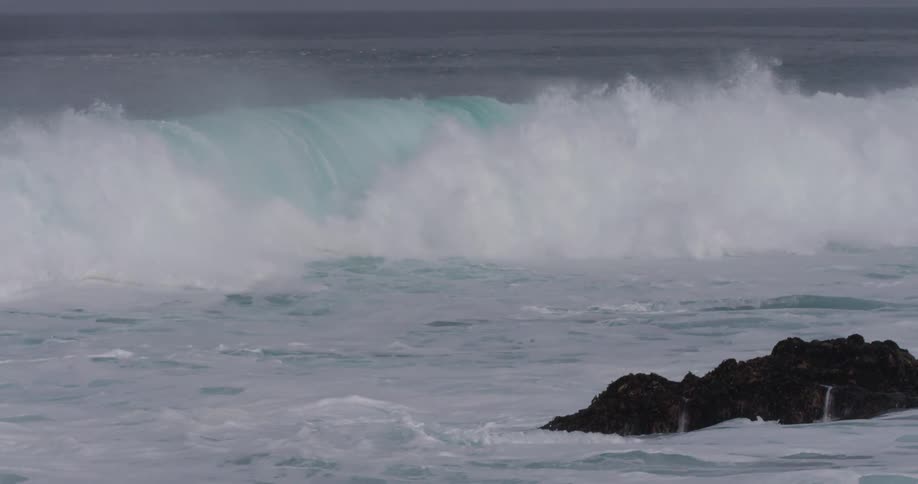 A large wave crashes against the rocky coast