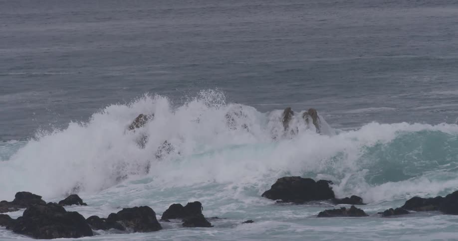 Ocean waves crash against a tall rocky island