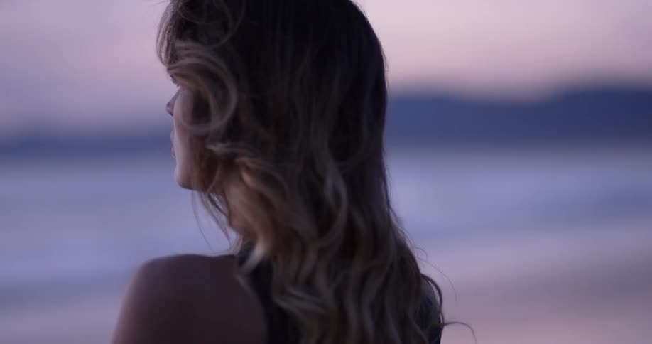 A woman standing on a beach looking out at the ocean in the evening