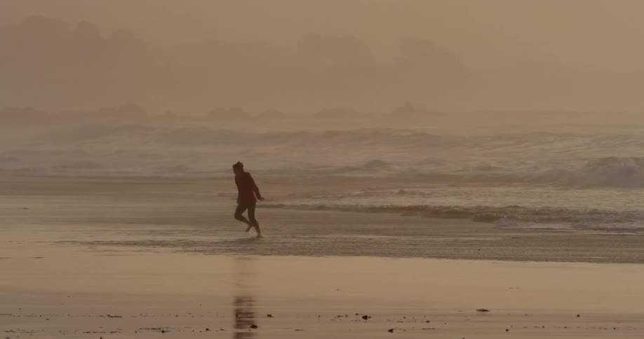 A woman runs around on the beach at sunset