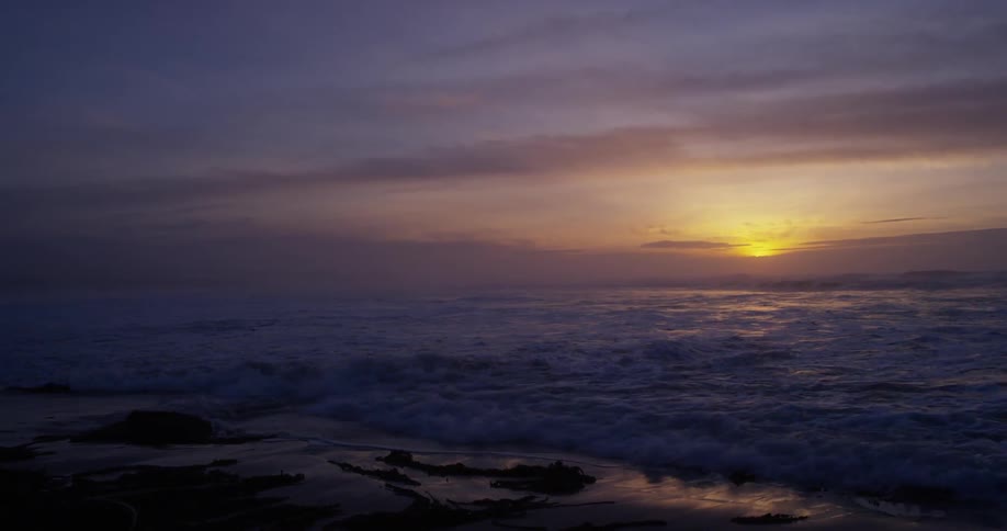 Waves crash on shore of beach at dusk