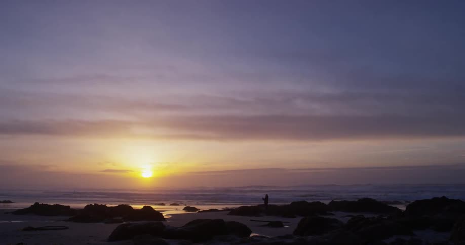 A person walks and stands on a rocky beach
