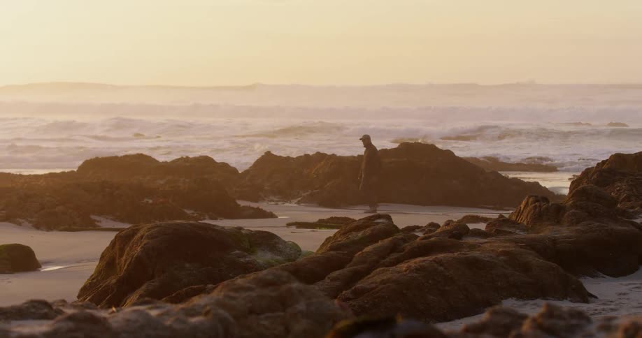 A man walks along the rocks on a beach