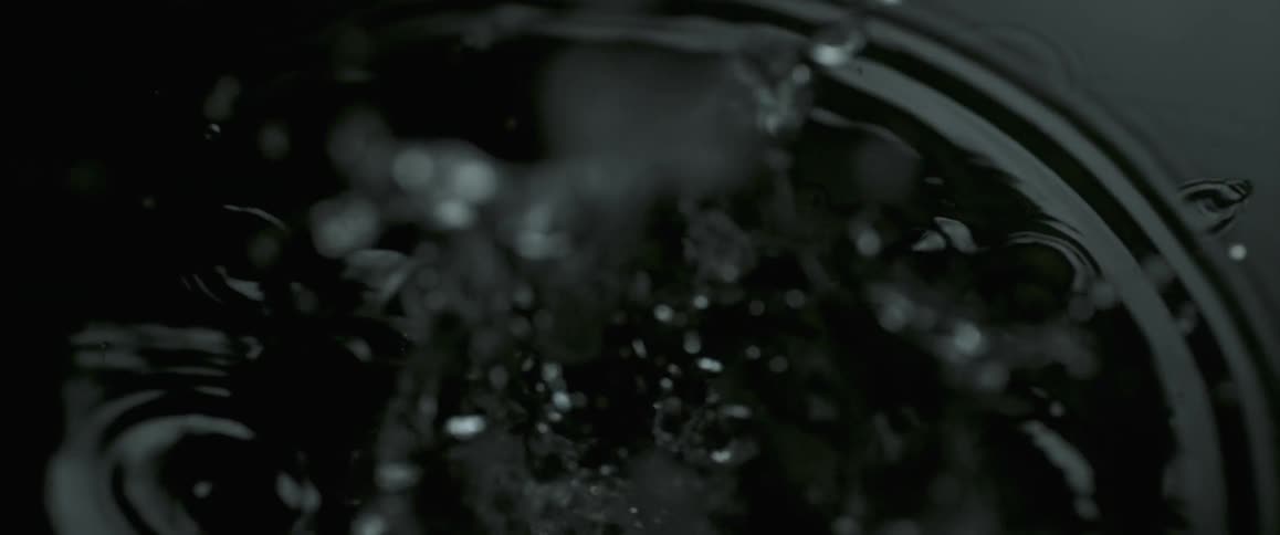 A slow-motion, close view of water droplets landing in a pool of water