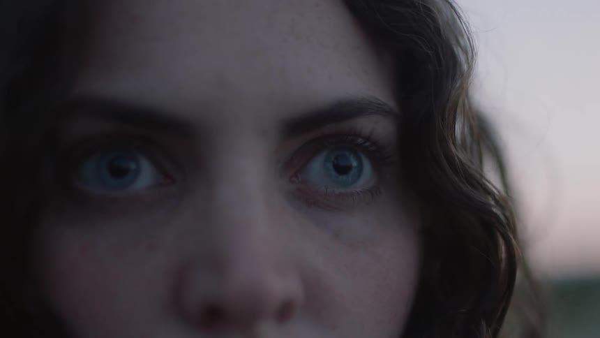 A woman opens her big blue eyes while standing outside at sunset