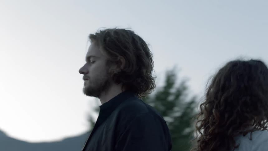 Fog floats around a man and woman standing outside back to back with their eyes closed