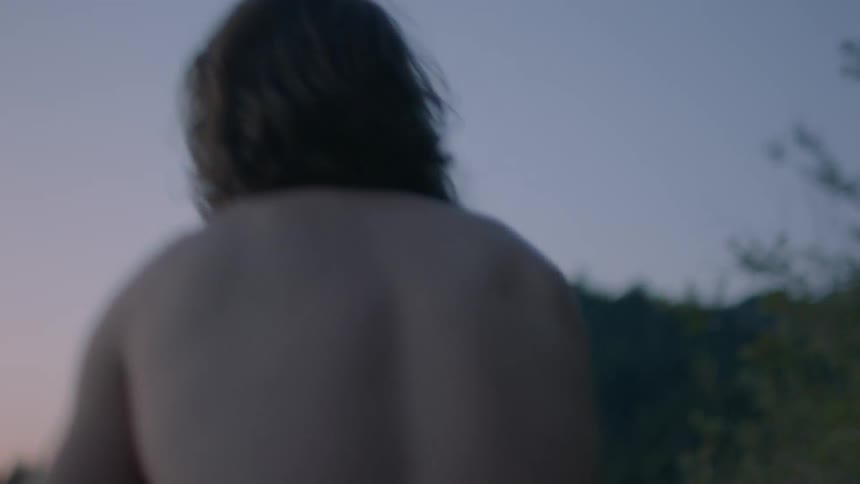 A caucasian male and female couple getting undressed and hugging on a shoreline