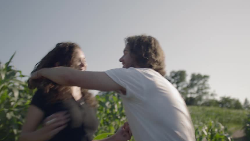 A couple walks through a field holding hands and hugging