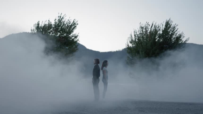 Man and woman standing back to back on a road covered in fog