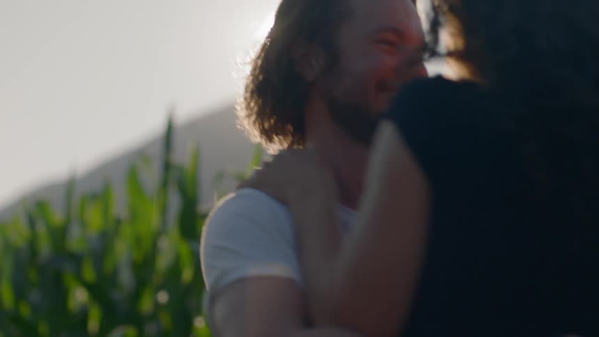 A woman runs into a mans arms near a corn field on a sunny day