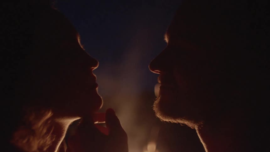 A man and woman looking into each others in front of a bonfire