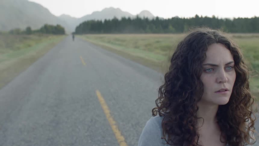 Two people walk away from each other on a rural two lane road then stop and look back